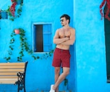 topless man in red shorts and white sneakers standing beside brown wooden bench