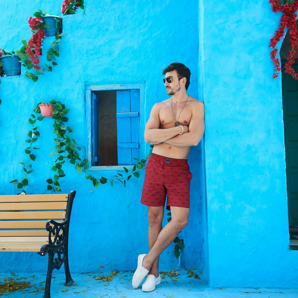 topless man in red shorts and white sneakers standing beside brown wooden bench