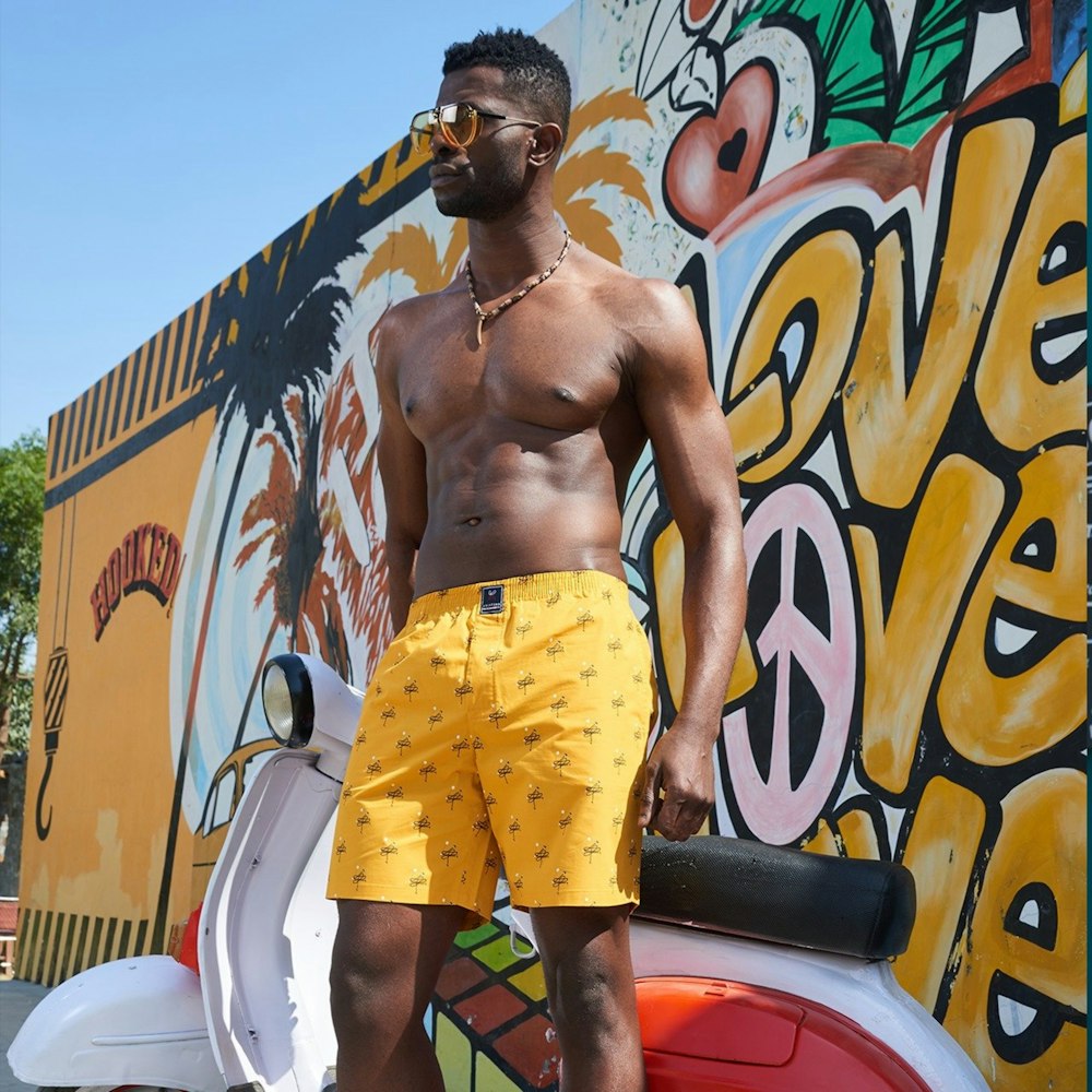 hombre en pantalones cortos amarillos y rojos de pie junto a la pared de graffiti durante el día