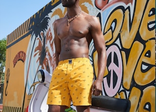 man in yellow and red shorts standing beside graffiti wall during daytime