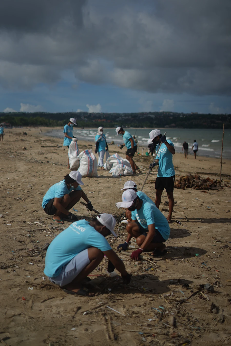 A clean-up crew working across a sunlit beach, bagging litter from the sand