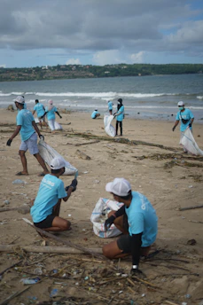 Volunteers collecting trash along a beach shoreline under a bright blue sky.