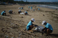Children and families participating in a beach cleanup event, with waves gently rolling in the background.