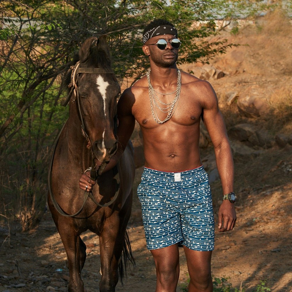 woman in blue and white floral skirt standing beside brown horse during daytime