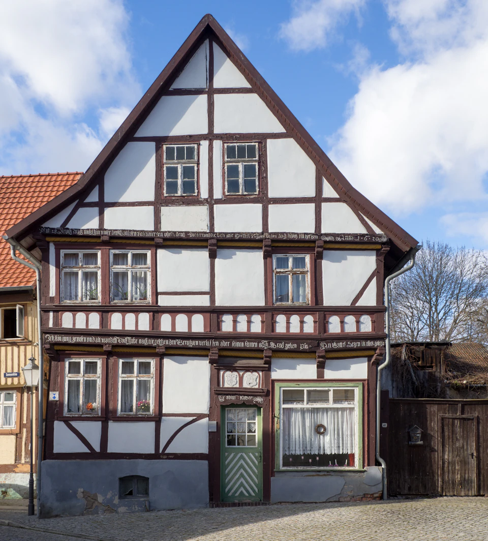 Two-story house with white facade and brown trim features triangular roof supported by wooden beams