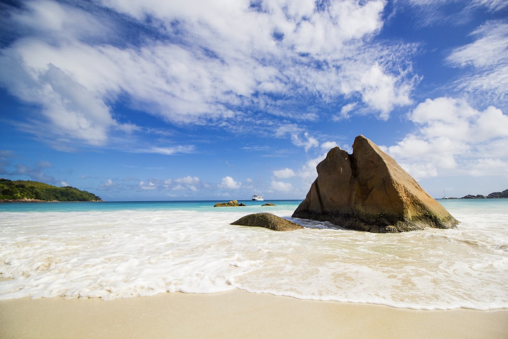 Formation rocheuse brune sur le bord de la mer sous un ciel nuageux ensoleillé bleu et blanc pendant la journée