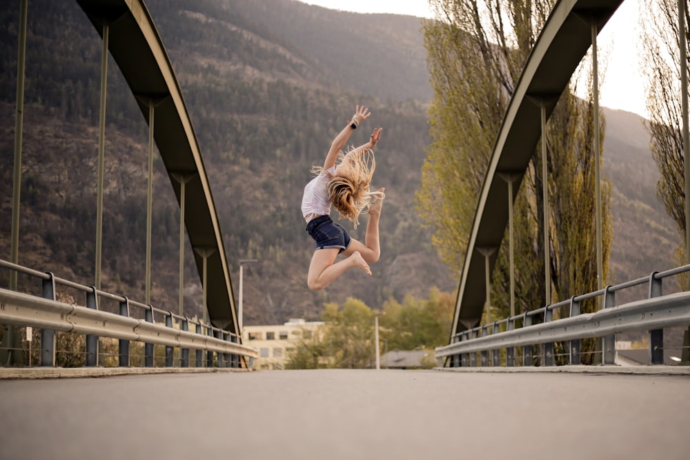 woman in blue denim shorts jumping on the bridge during daytime