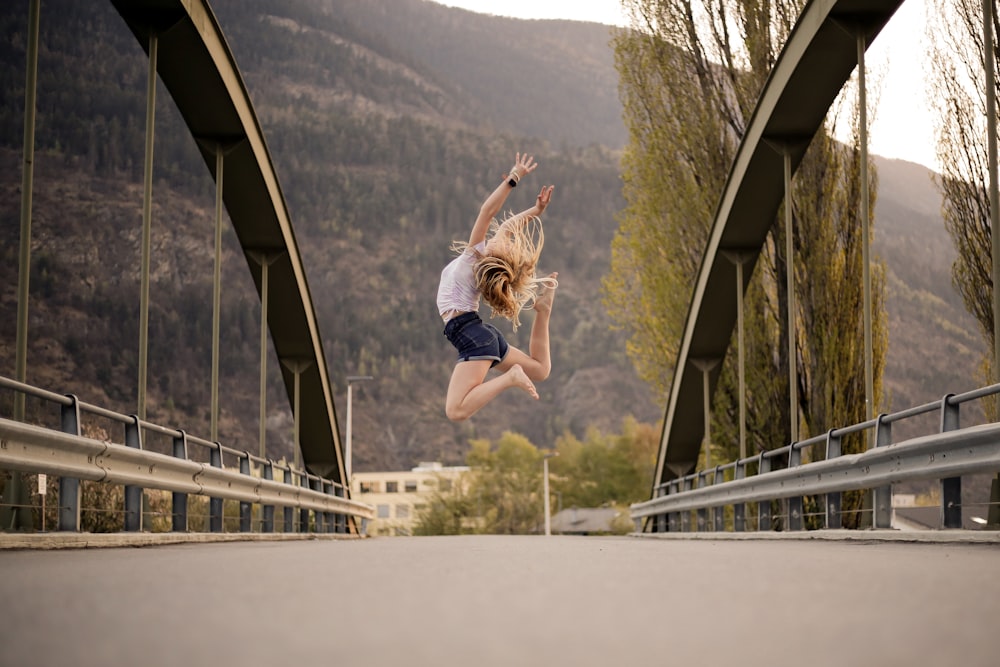 Frau in blauen Jeansshorts springt tagsüber auf die Brücke