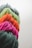 Bundles of yarn in vibrant pink, orange, green, and dark gray are arranged in a row. The texture of the yarn is soft and fibrous, with strands tightly wound together.