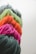 Bundles of yarn in vibrant pink, orange, green, and dark gray are arranged in a row. The texture of the yarn is soft and fibrous, with strands tightly wound together.