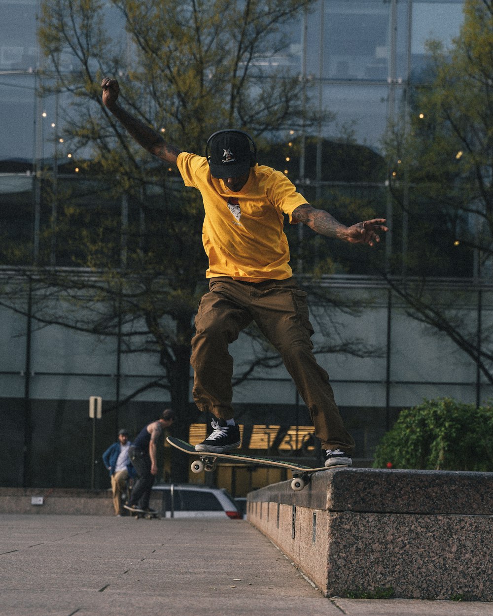 Mann in gelbem Hemd und brauner Hose spielt Skateboard