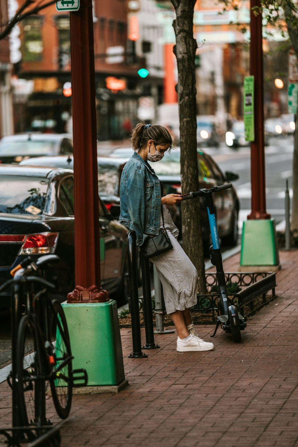 woman in blue denim jacket standing beside black bicycle during daytime