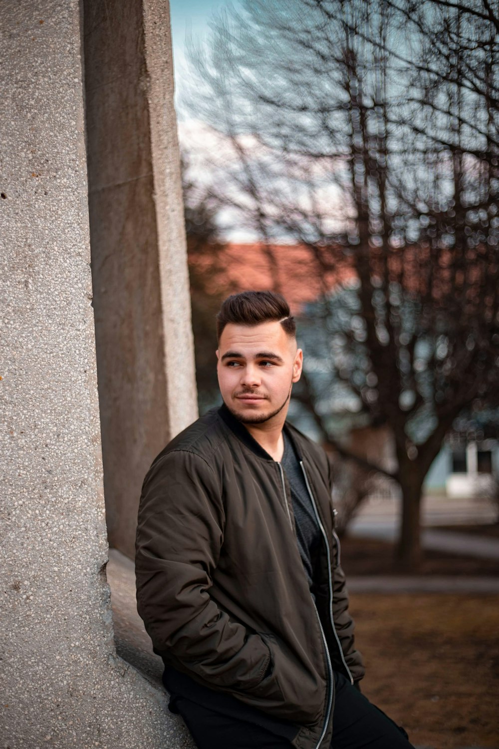 man in black leather jacket standing beside brown concrete wall during daytime