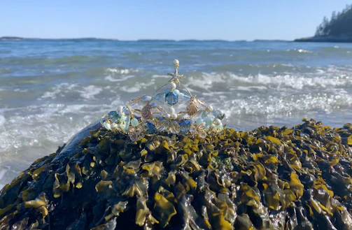 Hair jewelry pieces adorned with tiny crystals and shells, resting on a sandy shore.