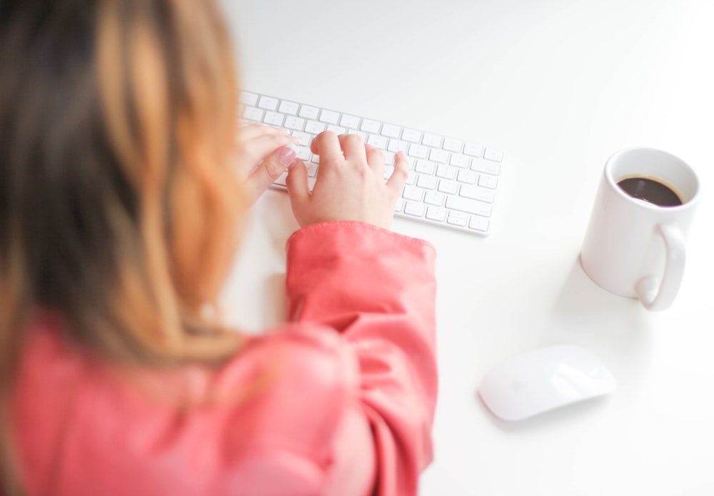 girl in pink long sleeve shirt using white computer keyboard