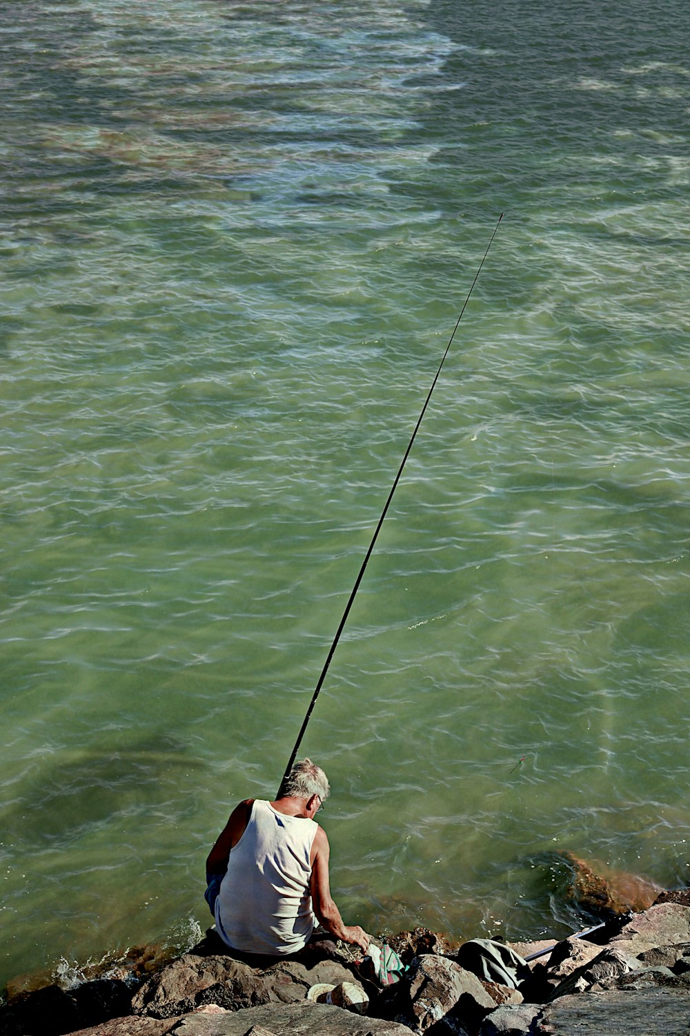 woman in white tank top and black shorts holding black fishing rod