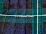 An elegant tartan quilt laid out on a wooden table with Scottish clan symbols embroidered.