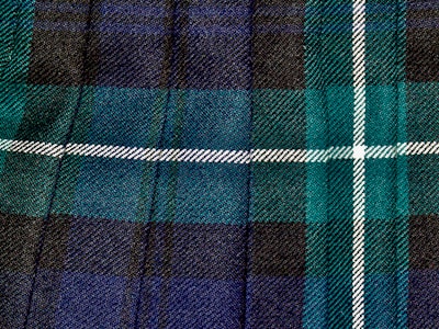 An elegant tartan quilt laid out on a wooden table with Scottish clan symbols embroidered.
