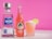 A bottle of 1800 Silver Tequila stands next to a Jarritos guava soda bottle, both placed on a marble surface. Beside them, a glass filled with a pink beverage, topped with coconut shavings and garnished with a lime slice. The background is a vibrant pink.