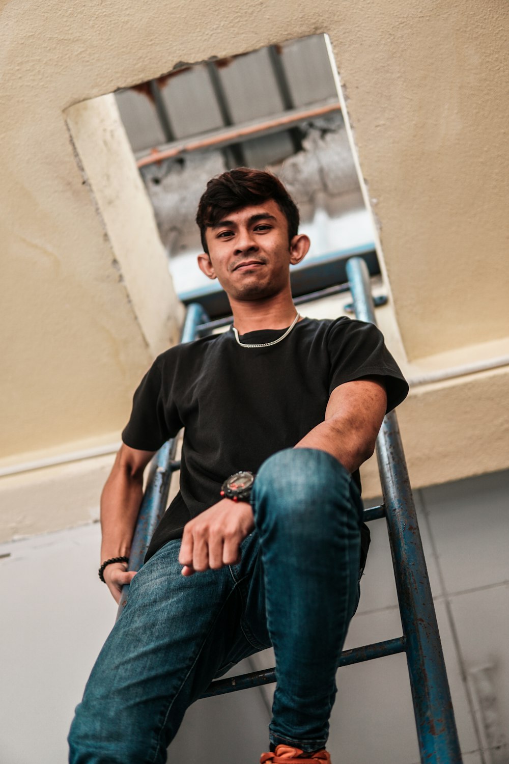 man in black crew neck t-shirt and blue denim jeans sitting on gray concrete stairs