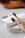 Two bamboo toothbrushes with black bristles are placed on rolled-up white towels. A sprig of rosemary adds a touch of greenery to the scene, and a wooden bowl is subtly visible in the blurred background.