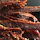 Close-up of a hand holding a crispy beef jerky strip with a rustic wooden background.
