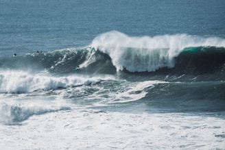 Large, powerful ocean waves crash with surfers riding some of them, showcasing skill and adventure amidst the vast expanse of blue water.