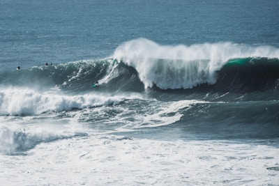 Large, powerful ocean waves crash with surfers riding some of them, showcasing skill and adventure amidst the vast expanse of blue water.