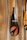 A close-up of a paddle with a shiny, carbon fiber-like blade featuring vibrant graphic designs and the word 'RUMO'. The blade design includes a circle with gradient colors of orange and blue, and a stylized arrow. The paddle's handle is wooden, and it is leaning against a textured wall.
