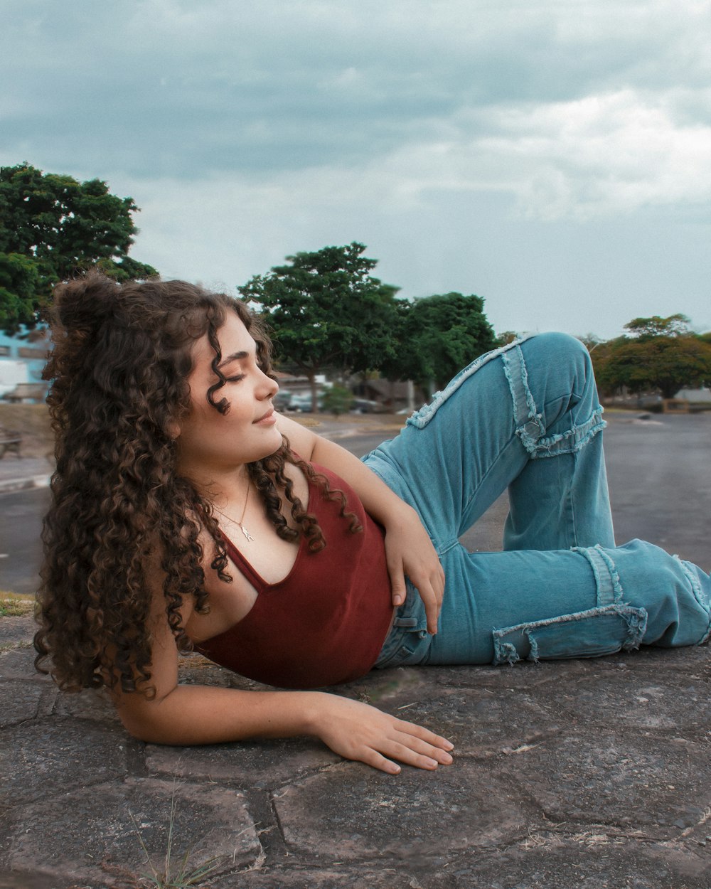 woman in red tank top and blue denim jeans sitting on gray concrete floor during daytime