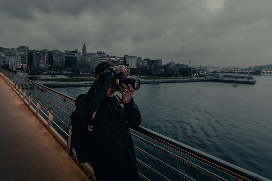 man in black jacket and black cap standing on bridge