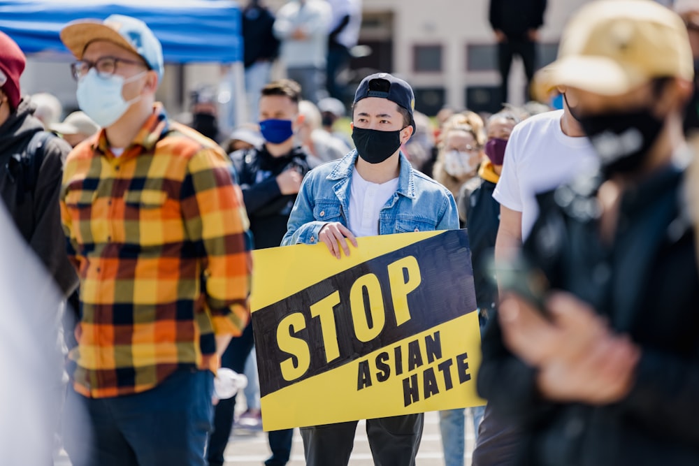 a man wearing a face mask holding a stop asian hate sign