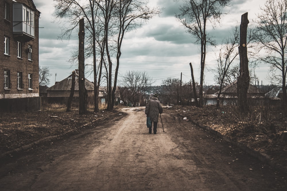 homme en veste grise marchant sur un chemin de terre pendant la journée