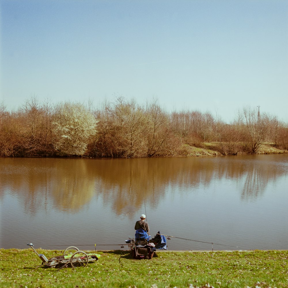 man in red jacket sitting on brown wooden bench near lake during daytime