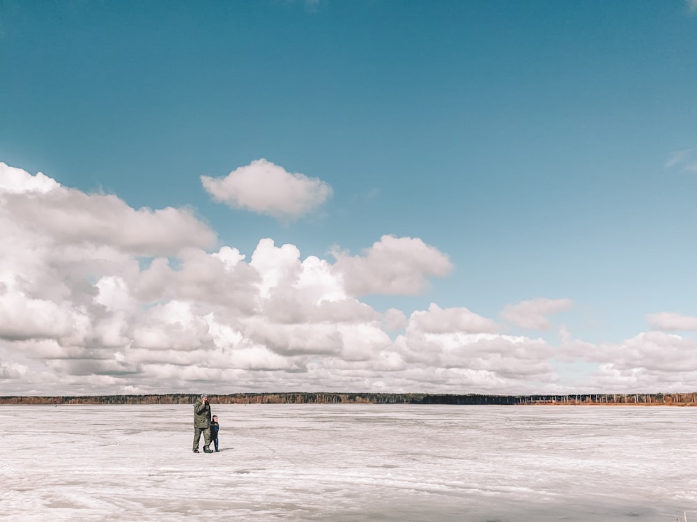 2 Personen stehen tagsüber auf schneebedecktem Feld unter blau-weißem bewölktem Himmel