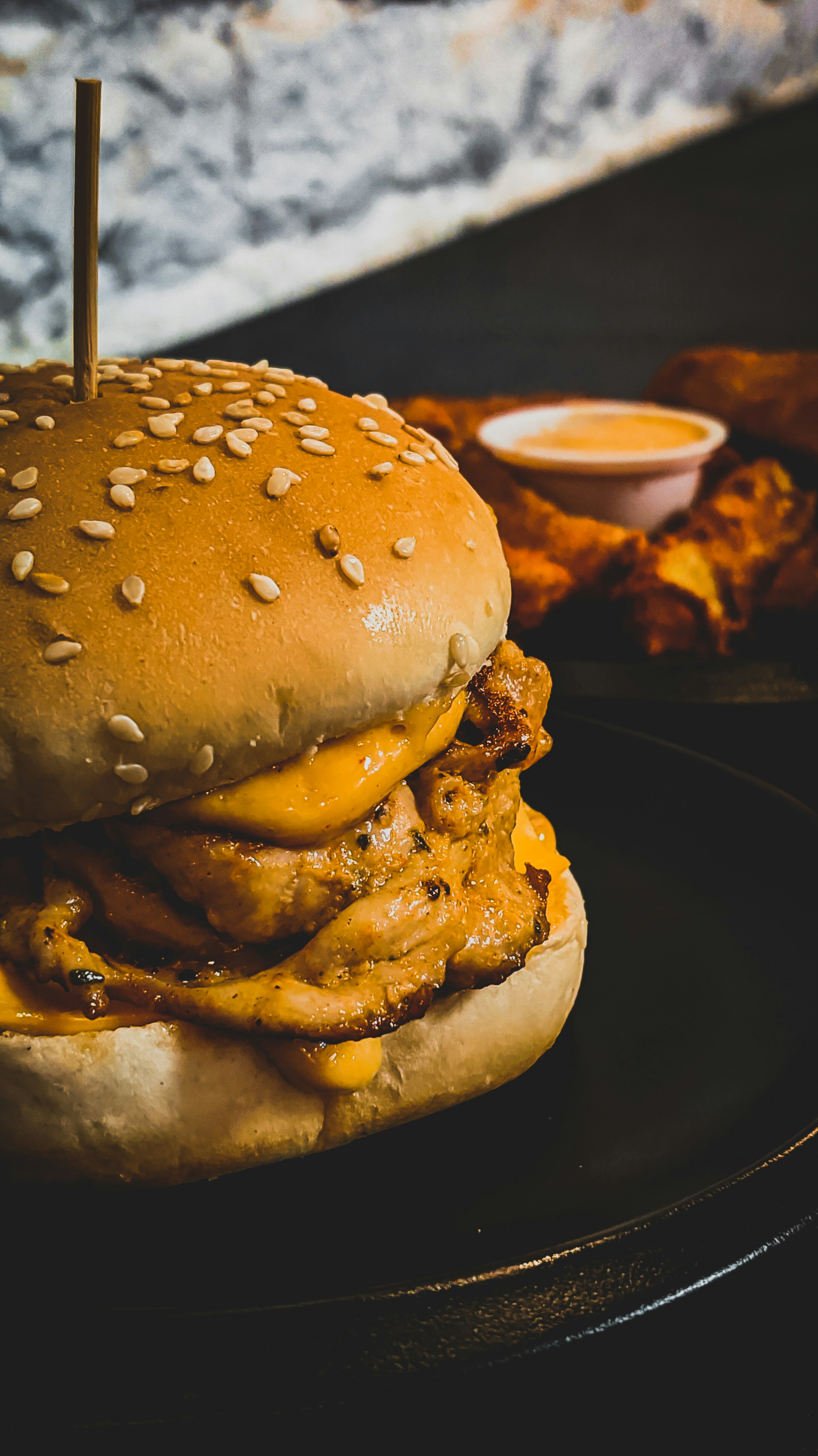Tall stacked double beef burger with melted yellow cheese and sesame bun on dark background