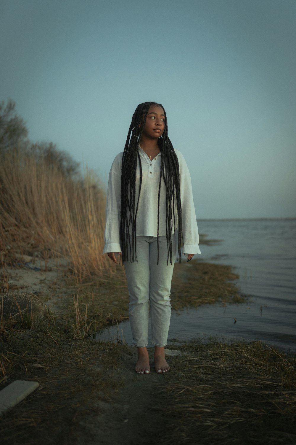 woman in white long sleeve shirt and white pants standing on brown field near body of during