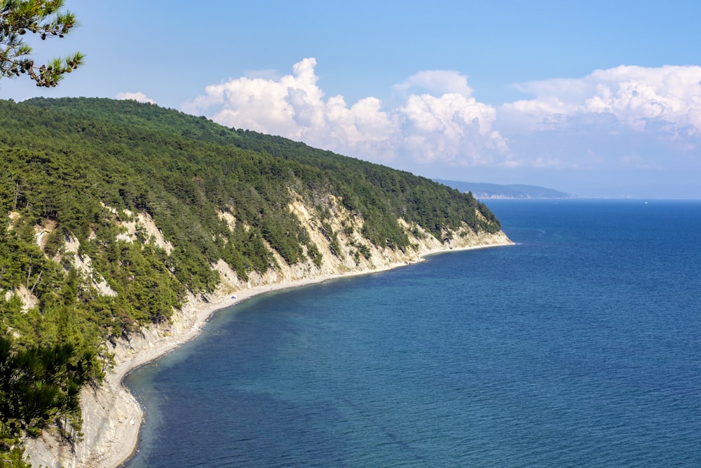 green and brown mountain beside blue sea under blue and white cloudy sky during daytime