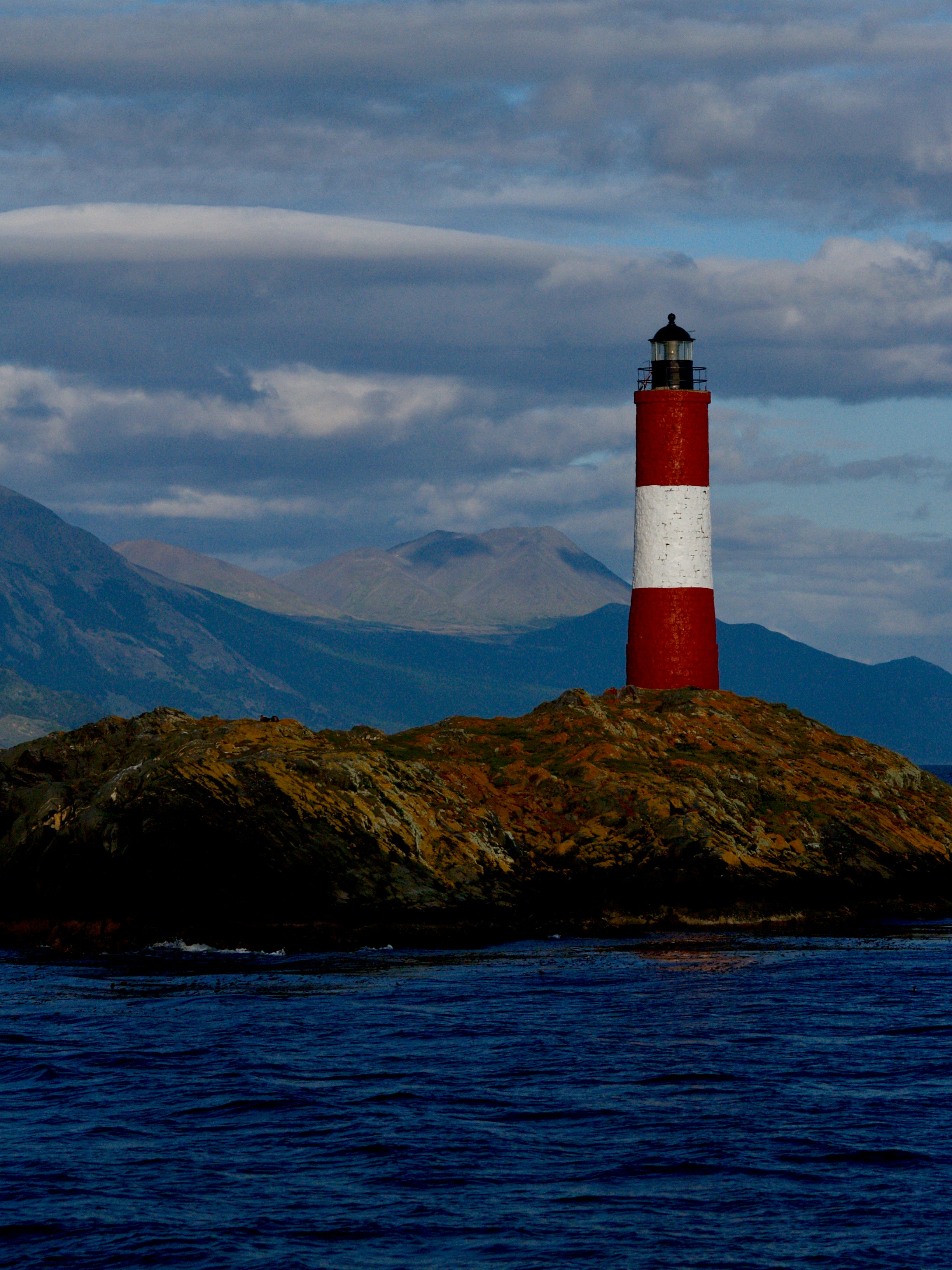 red and white lighthouse on brown and green mountain under white clouds and blue sky during