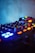 A close-up view of a sound mixing console with various knobs and buttons illuminated in blue and orange lights. The background is blurred, creating a focus on the equipment with an atmospheric and moody lighting setup.