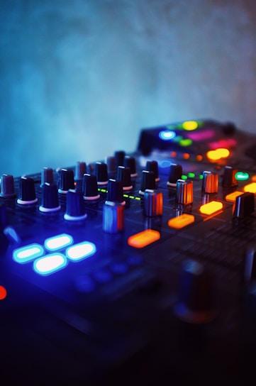 Close-up of a mixing console illuminated by deep blue LED lights with a blurred waveform in the background.