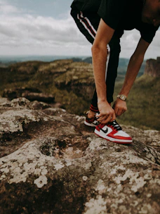A traveler lacing up running shoes beside a scenic mountain trail at sunrise.