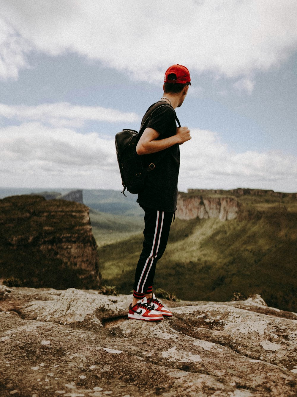 homem de camiseta preta e calças pretas vestindo sapatos nike vermelhos e brancos em pé sobre on on on