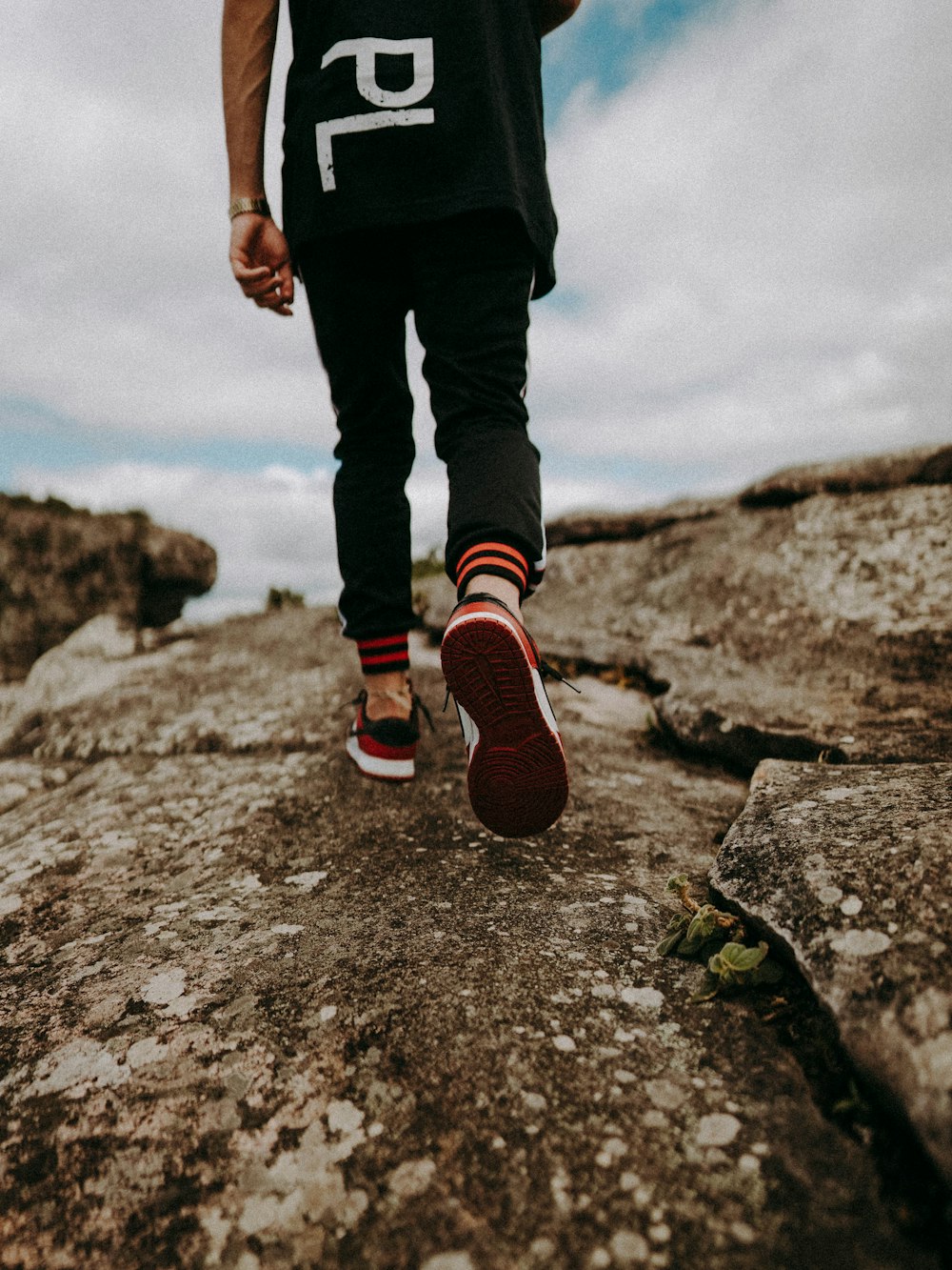 person in black pants and red and white sneakers standing on gray rock during daytime