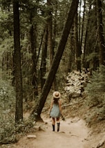 woman in white long sleeve shirt and blue denim jeans walking on forest during daytime