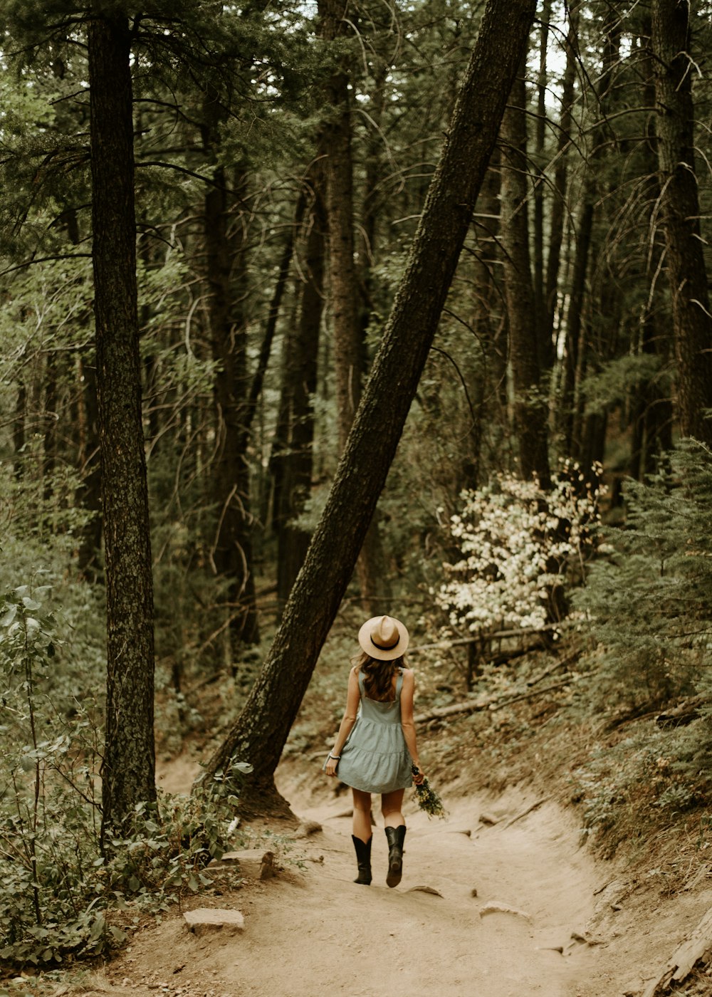 woman in white long sleeve shirt and blue denim jeans walking on forest during daytime