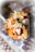 A close-up view of a spoon filled with assorted dried fruits and nuts, including almonds, cashews, pumpkin seeds, and dried cherries. The spoon is in focus with a blurred decorative background.