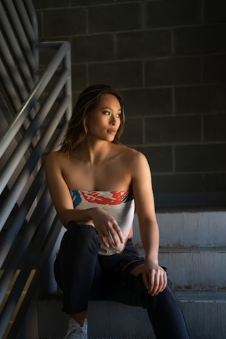 woman in red and white tube top and blue denim jeans sitting on stairs