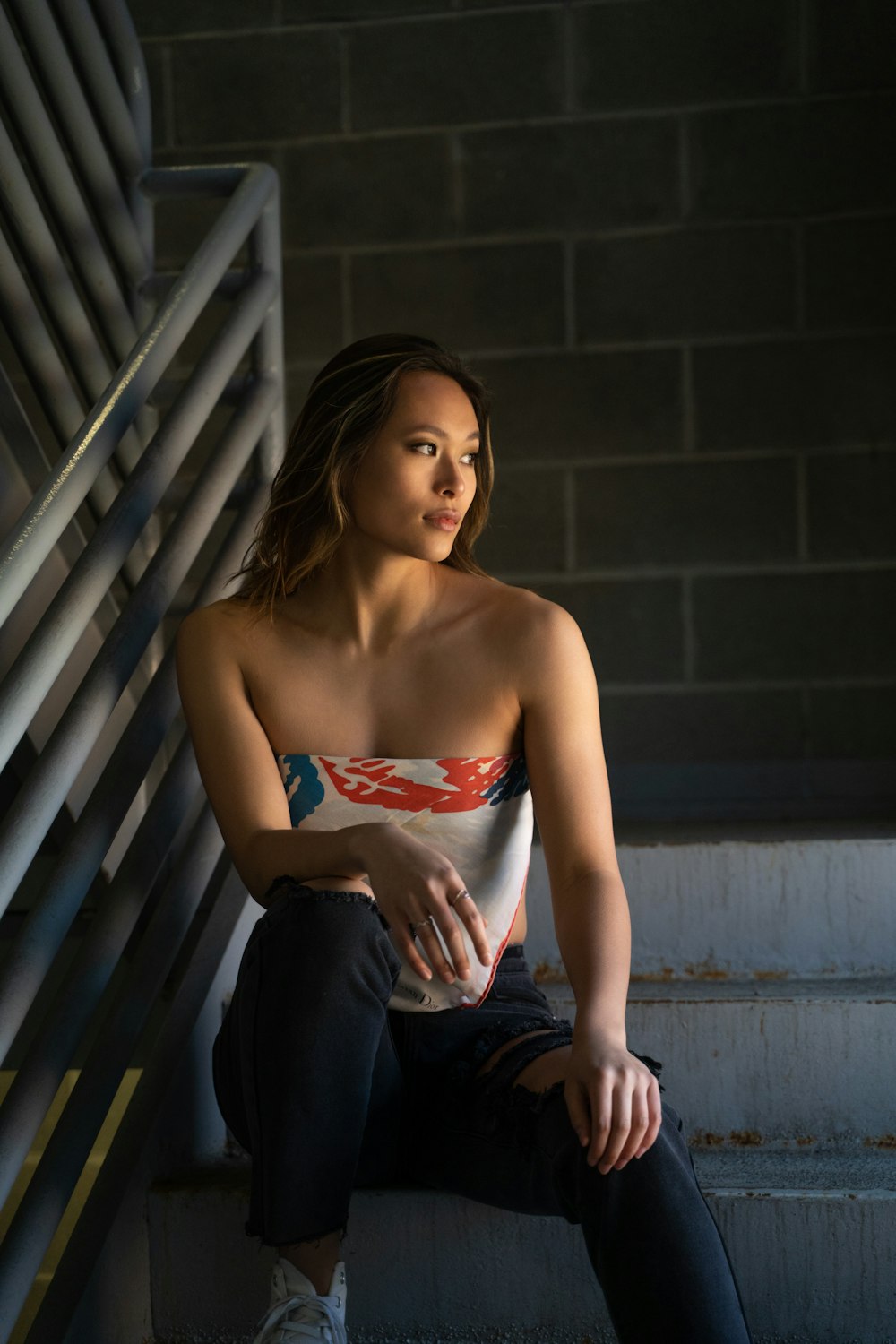 woman in red and white tube top and blue denim jeans sitting on stairs