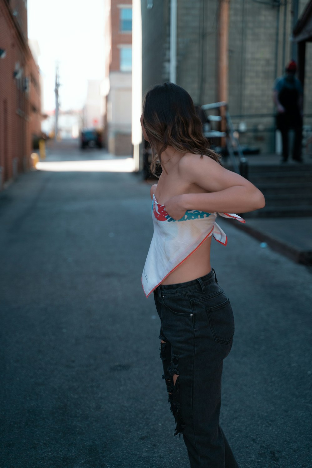 woman in white and red floral lace brassiere and black denim jeans standing on sidewalk during